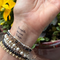 A close-up of a person's wrist wearing multiple beaded bracelets and a 'thoughts become things' temporary tattoo.
