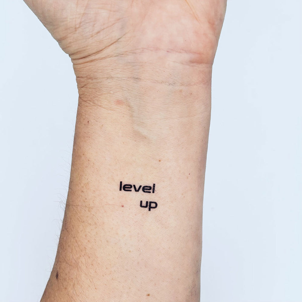 Level Up motivational temporary tattoo on inner forearm, minimalist design by Motivink, plain white background.