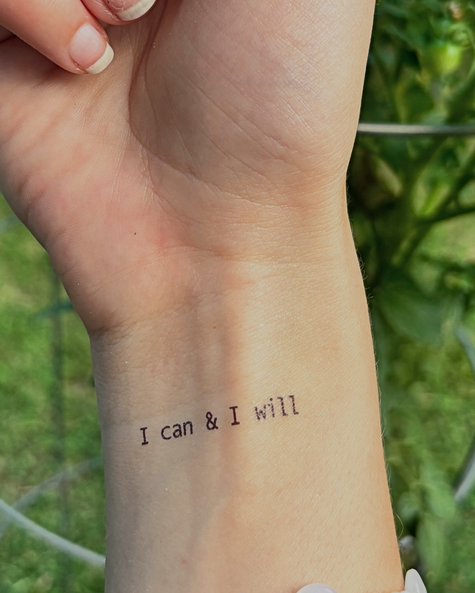 Hand with a tattoo of 'I can & I will' on a blurred green background
