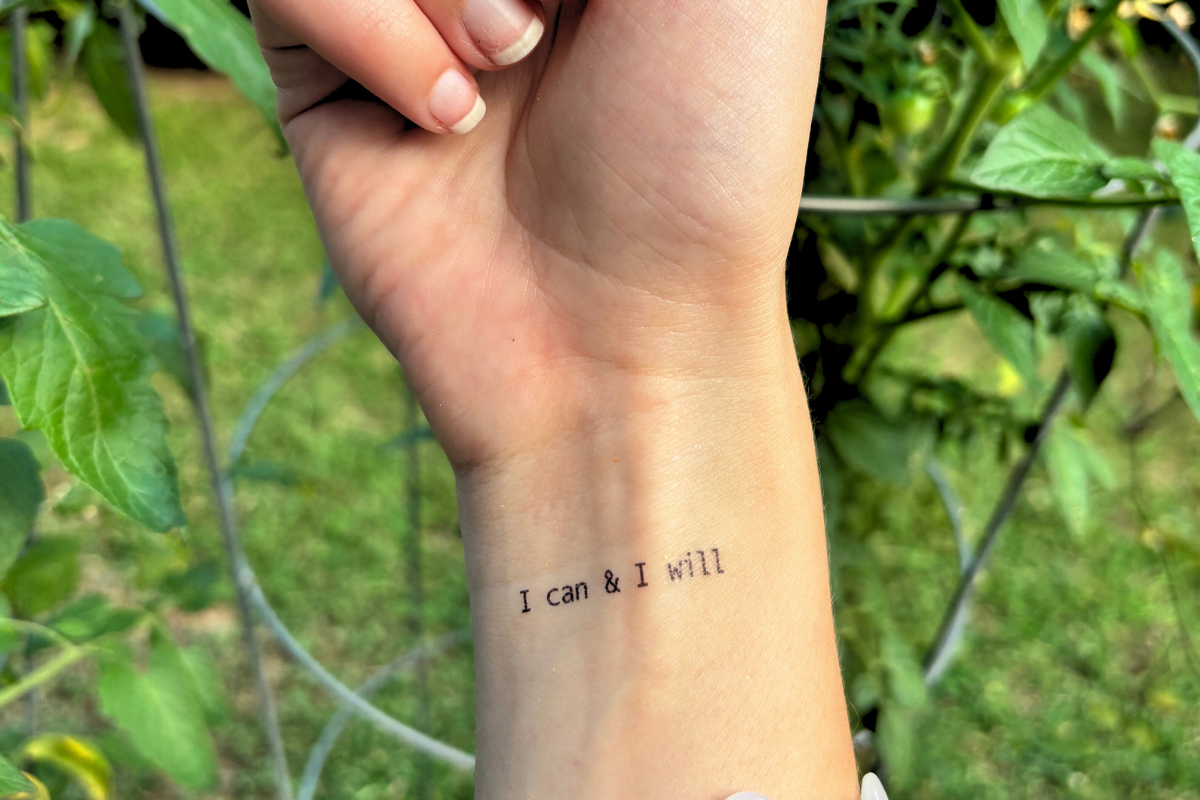 Hand with a temporary tattoo 'I can & I will' against a green outdoor background.