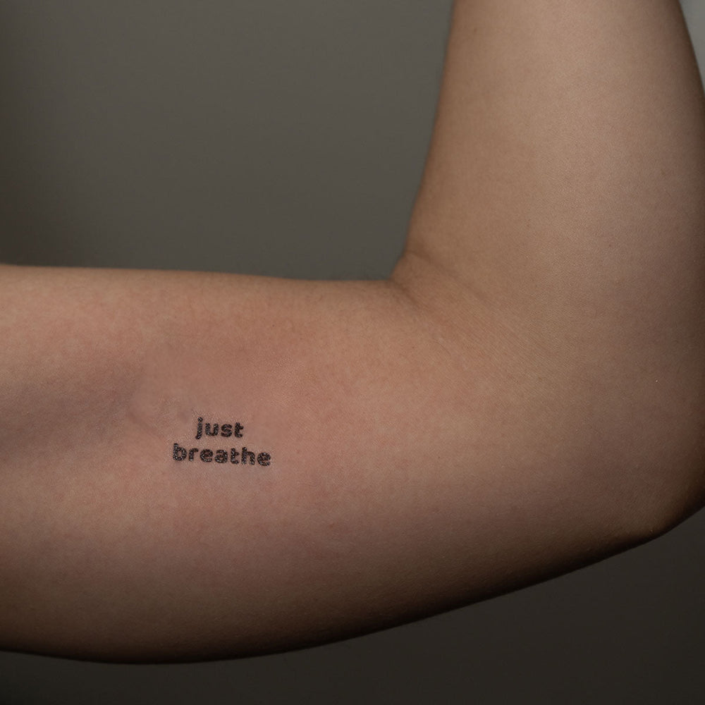 Just Breathe calming quote tattoo on bicep – for mindfulness and inner peace