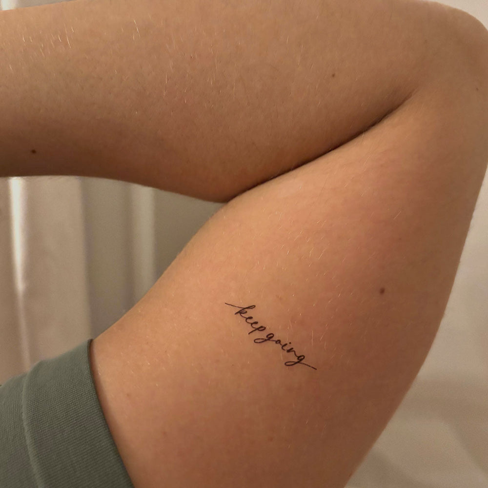 'keep going' inspirational temporary tattoo on bicep, fine line black tattoo mantra