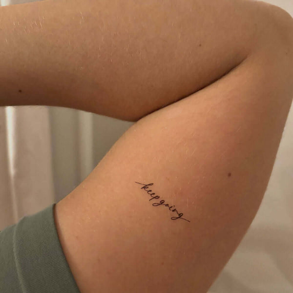 'keep going' tattoo on bicep, fine line black tattoo mantra -MotivInk