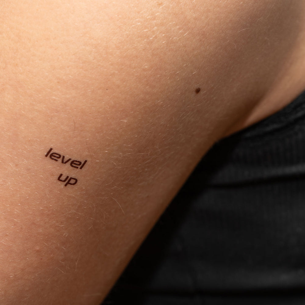 Level Up motivational temporary tattoo on upper arm, bold minimalist design.