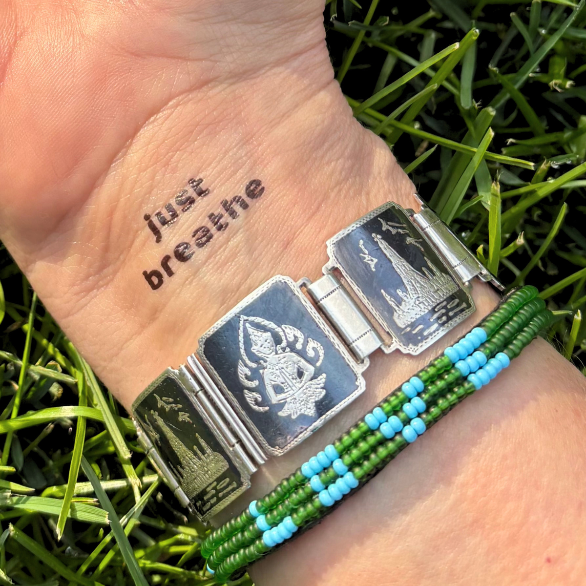 Just Breathe temporary tattoo on an inner wrist next to two bracelets