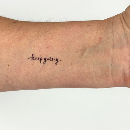 Tattoo of 'keep going' on a person's arm with a white background
