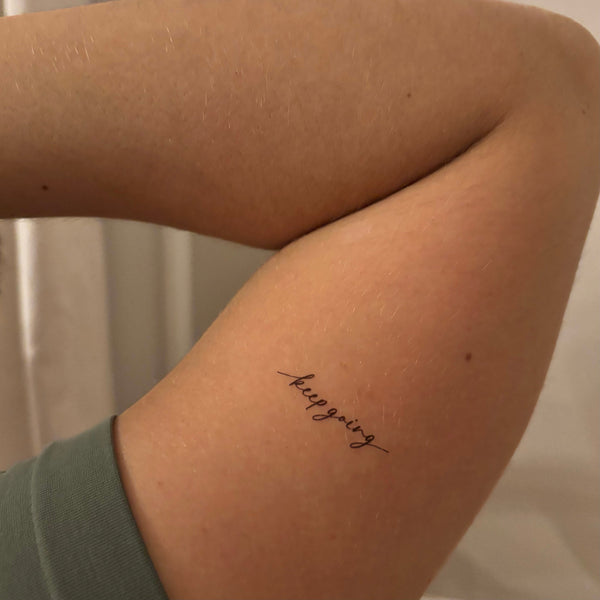 Small tattoo on a person's arm with the word 'keep going' against a neutral background