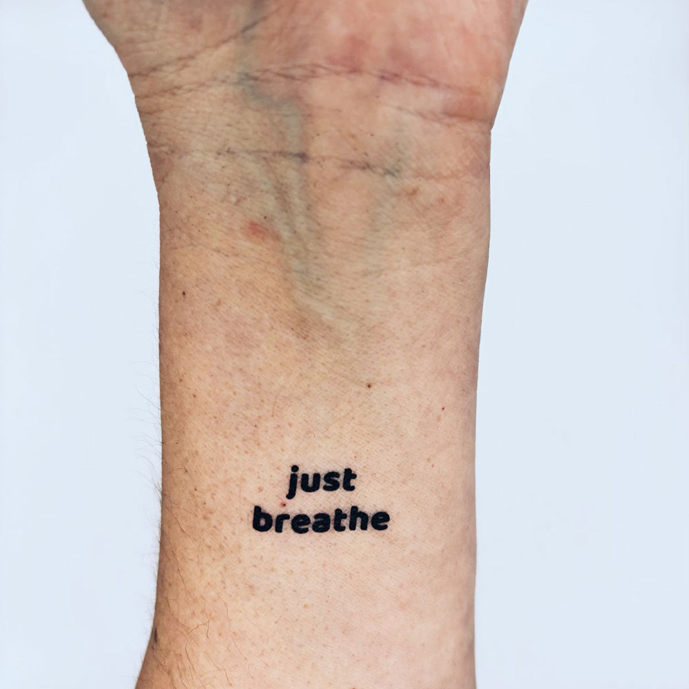 Just Breathe calming temporary tattoo mantra on inner forearm, bubble font black ink design by Motivink for inner peace