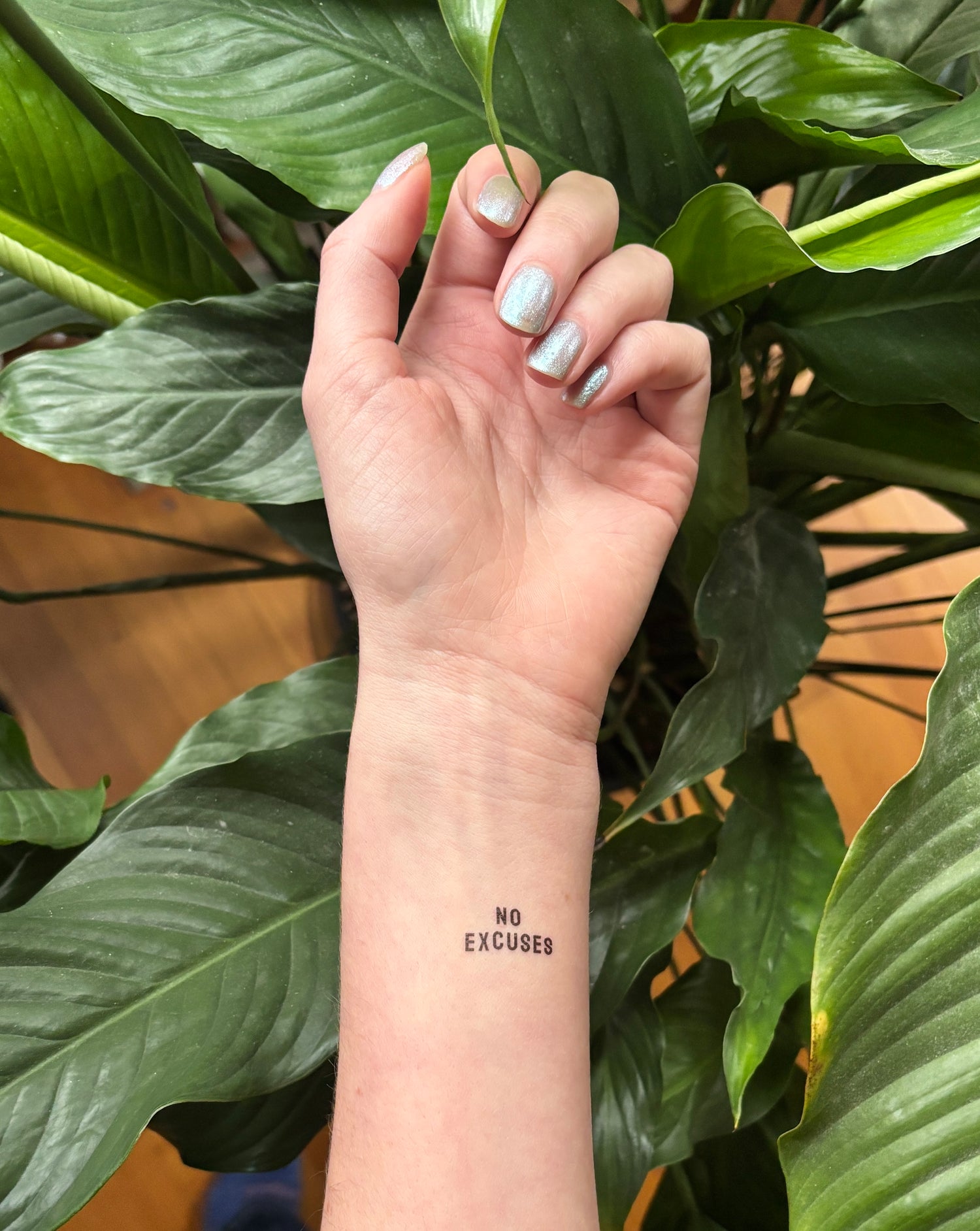 Hand with a tattoo of 'No Excuses' against a green leafy background