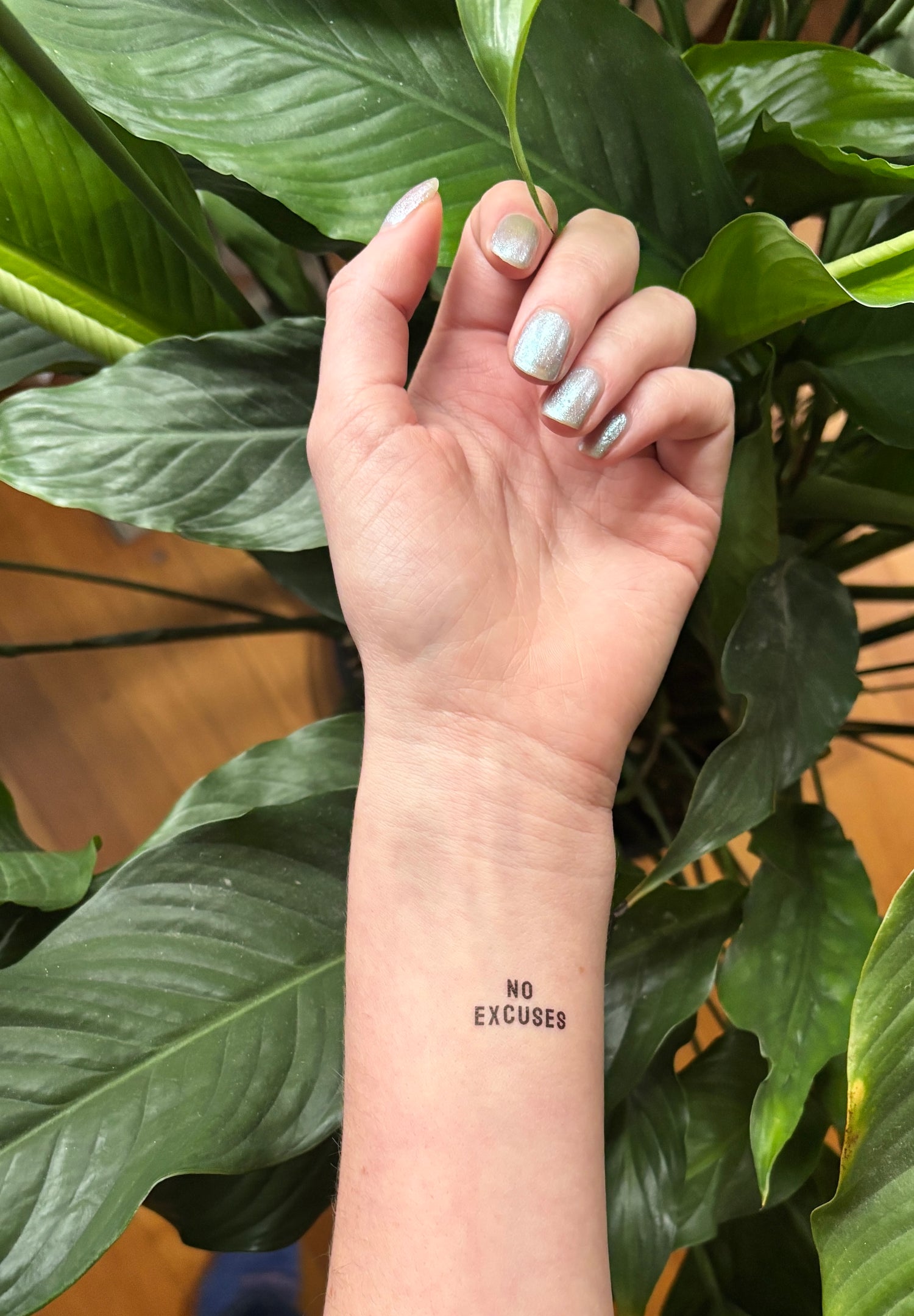 Hand with 'No Excuses' tattoo in front of green leaves
