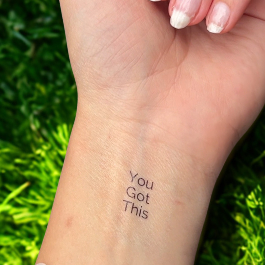 Hand with a tattoo 'You Got This' against a green grass background