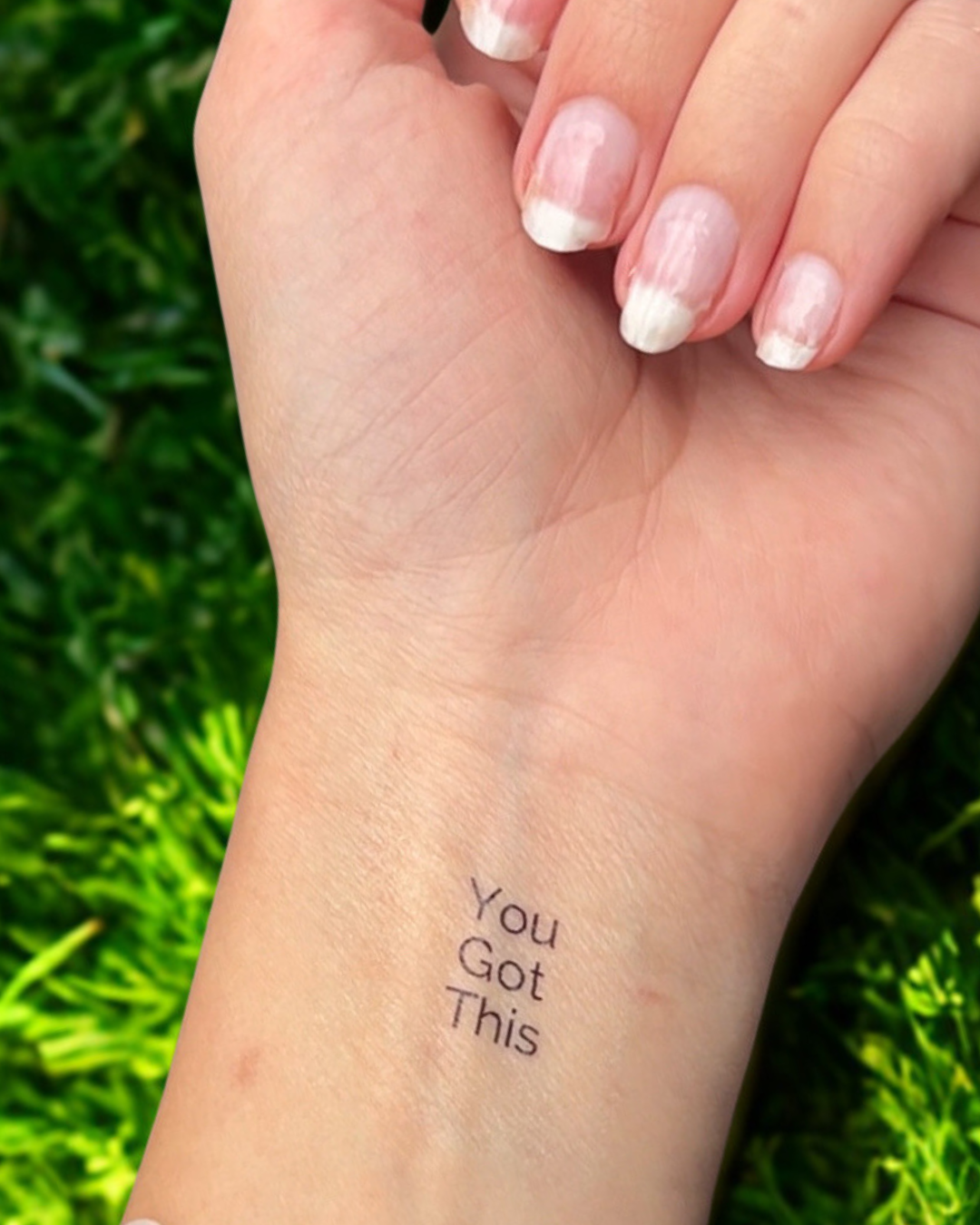 Hand with 'You Got This' tattoo on wrist against a green outdoor background