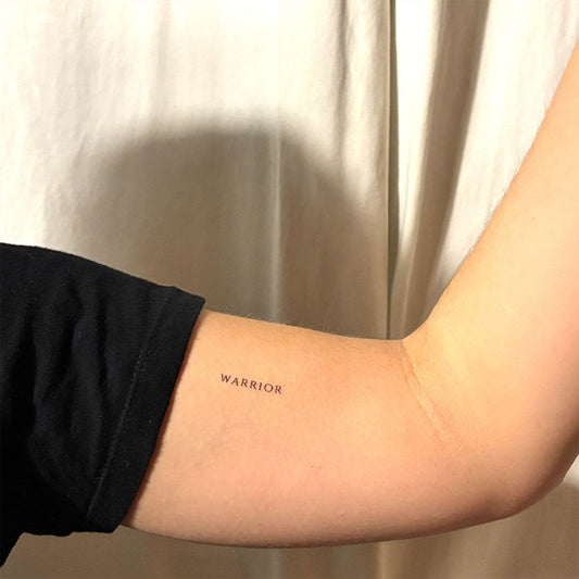 Black ink ‘WARRIOR’ motivational temporary tattoo on inner arm – minimalist quote design for strength, self-belief, and empowerment by MotivInk